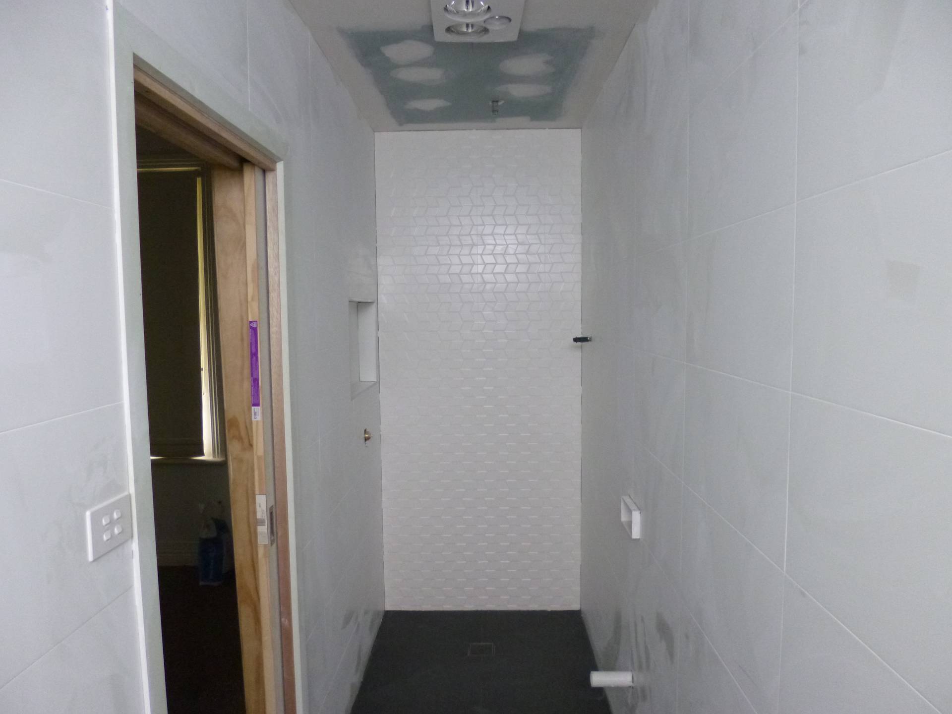 Floor to ceiling wall tiling completed with a tile shower base, feature tile to shower wall and a recessed shower niche .